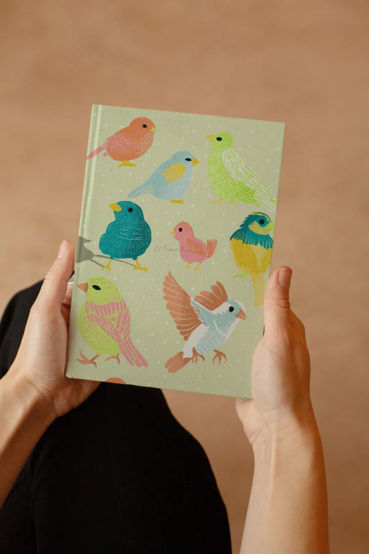 Woman holding a journal featuring the Flock Together bird illustration from a licensable surface pattern collection.