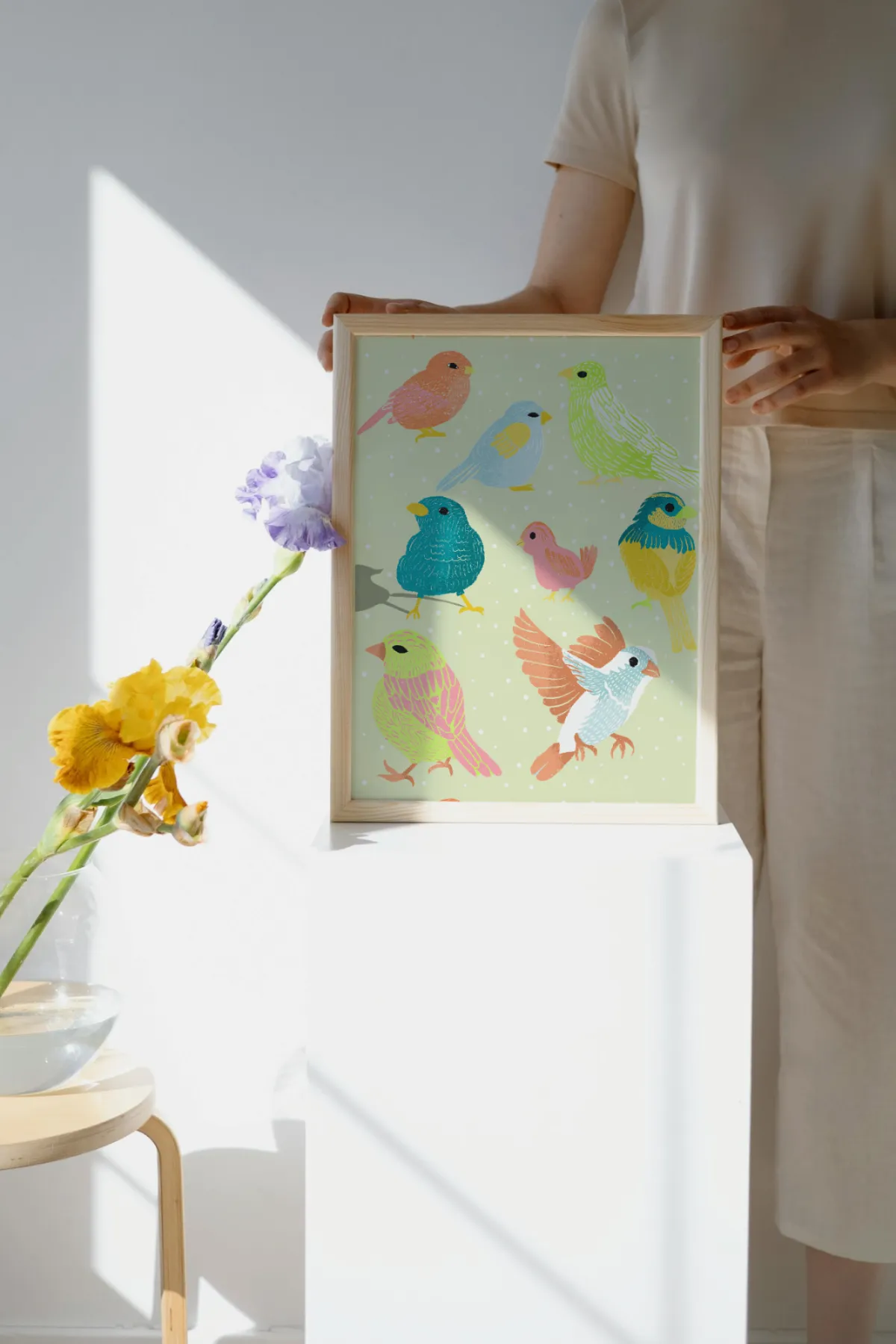 Woman holding a framed art print of the Flock Together bird illustration.