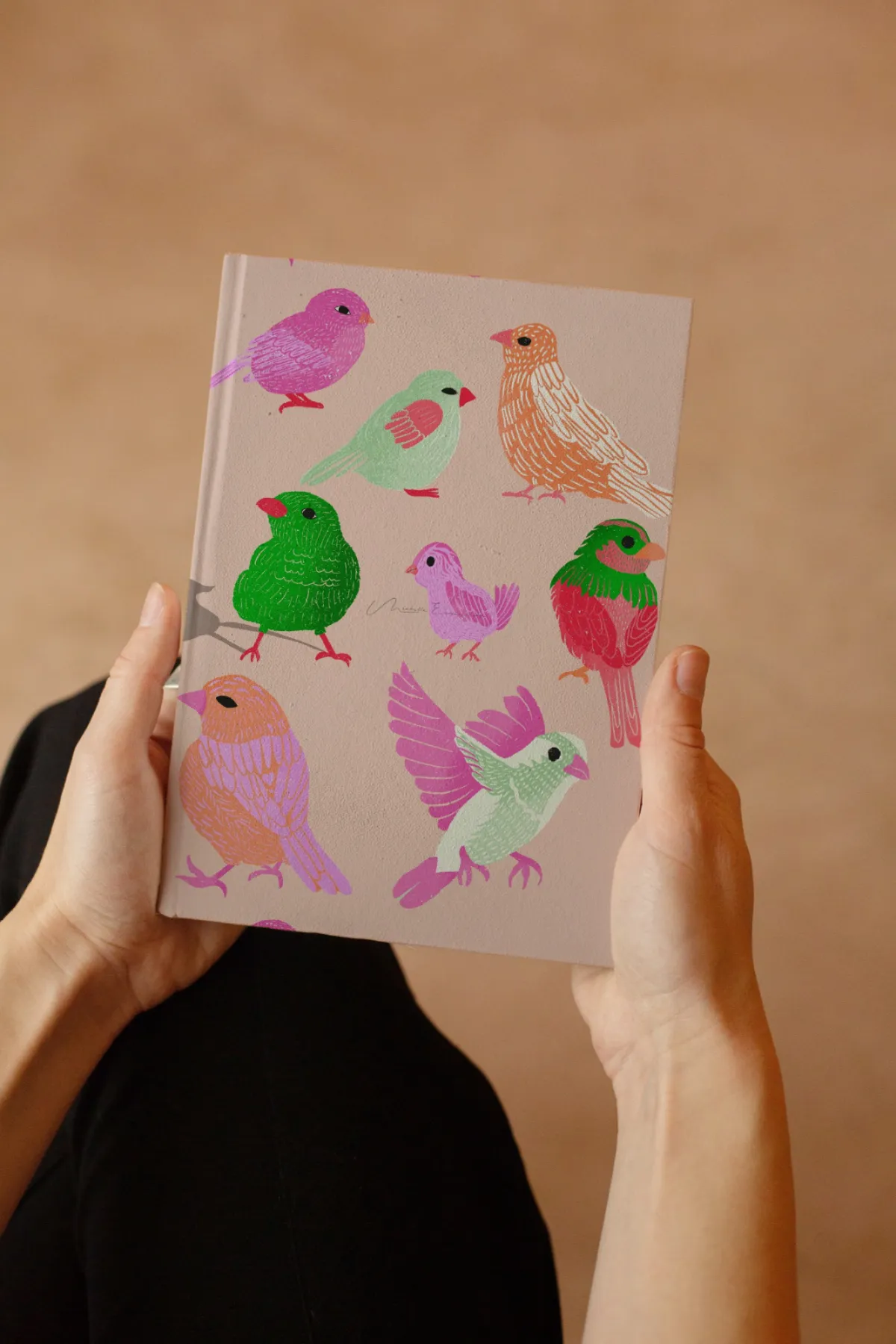 Woman holding a journal featuring the Flock Together bird illustration from a licensable surface pattern collection.
