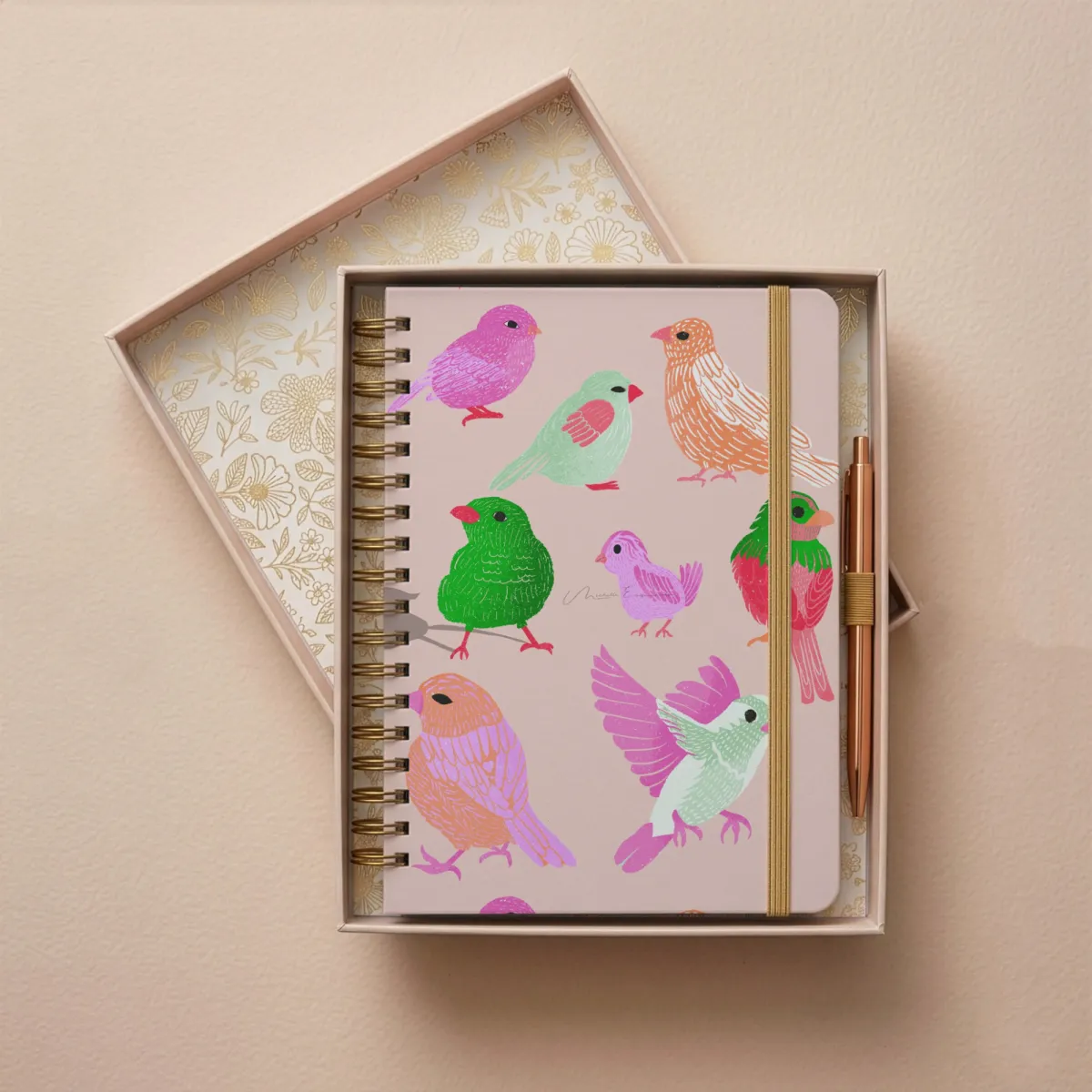 Closed gold ring spiral notebook with the Flock Together bird illustration cover design, shown on a table.