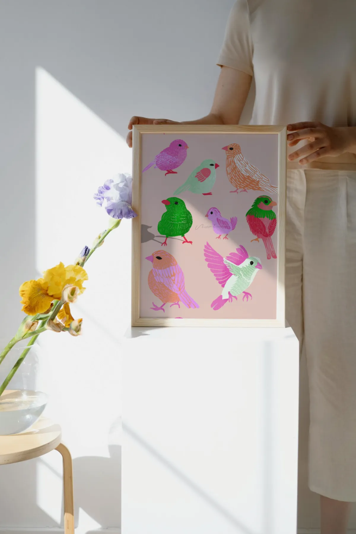 Woman holding a framed art print of the Flock Together bird illustration.