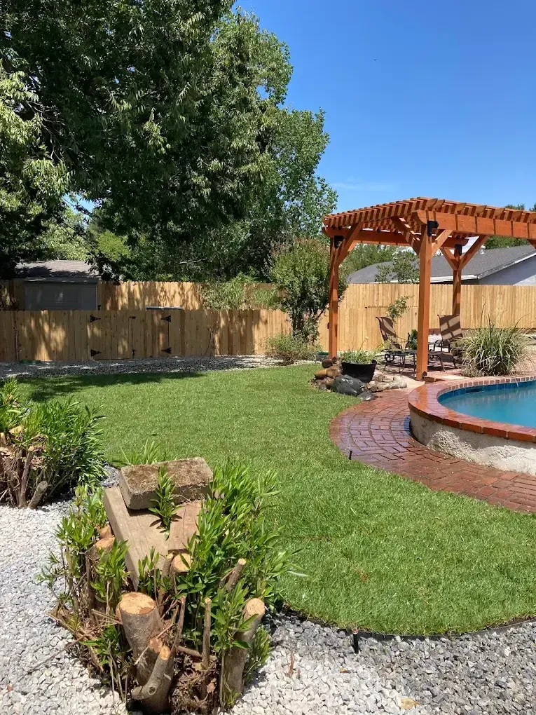 Backyard landscaping in Redding CA with lawn, pergola seating area, gravel borders, planting beds, and poolside brick patio by Outdoor Artisans