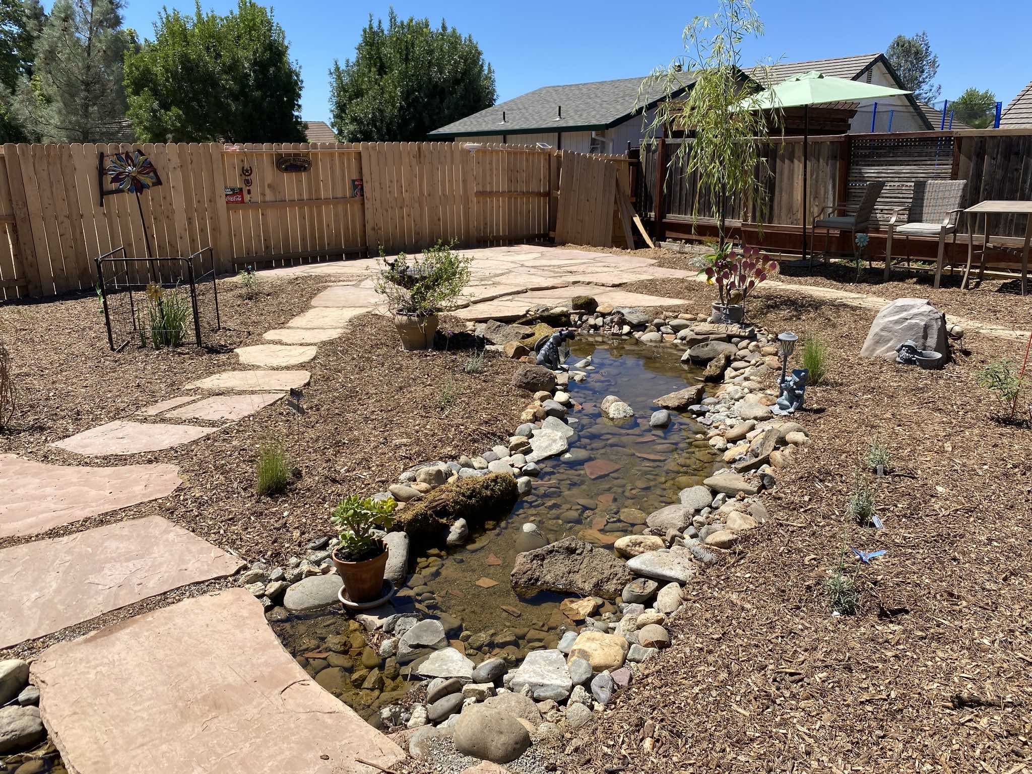 Backyard landscaping in Redding CA with flagstone pathway, rock-lined creek bed, mulch ground cover, and drought-tolerant planting by Outdoor Artisans