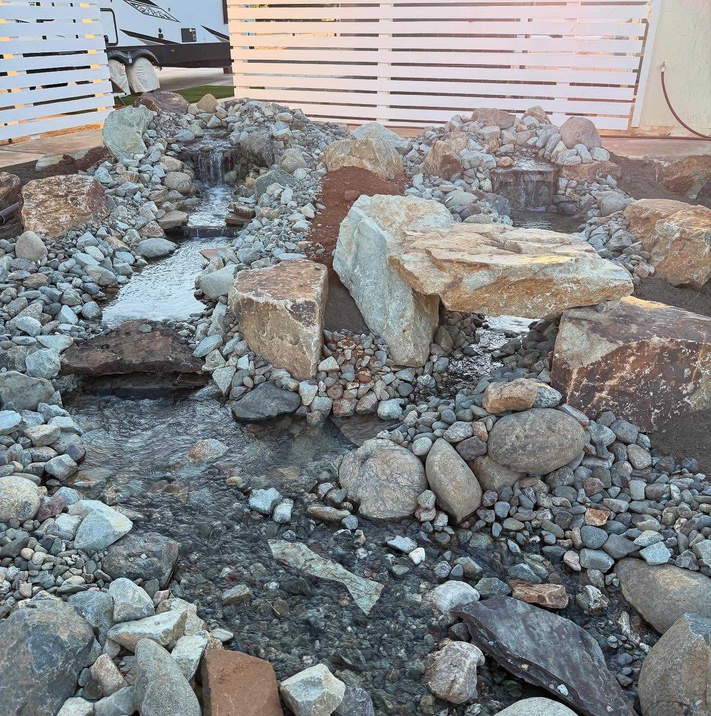 Backyard creek bed and waterfall landscaping in Redding CA with boulders, flowing water, and natural rock placement by Outdoor Artisans