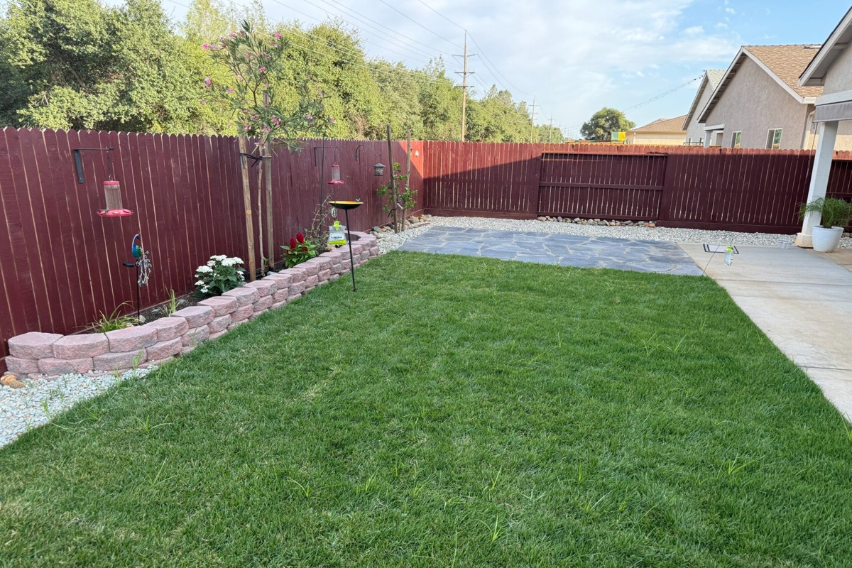 Stained wood privacy fence surrounding landscaped backyard with lawn and patio area