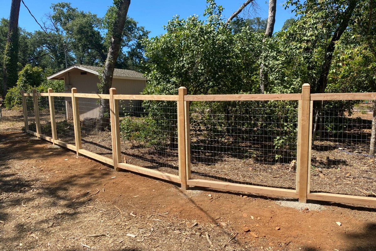 Custom wood and wire fence installation with posts and mesh panels for backyard enclosure