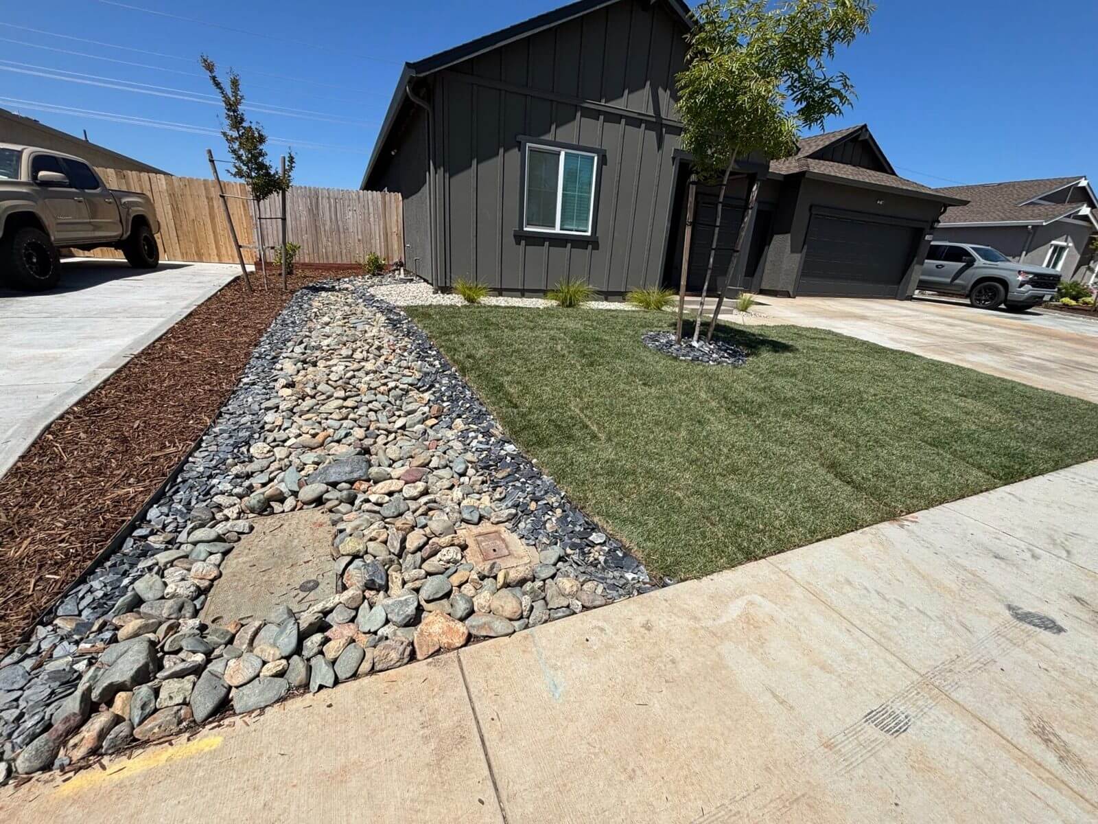 Front yard sod installation in Redding, CA with river rock drainage feature and clean lawn edges