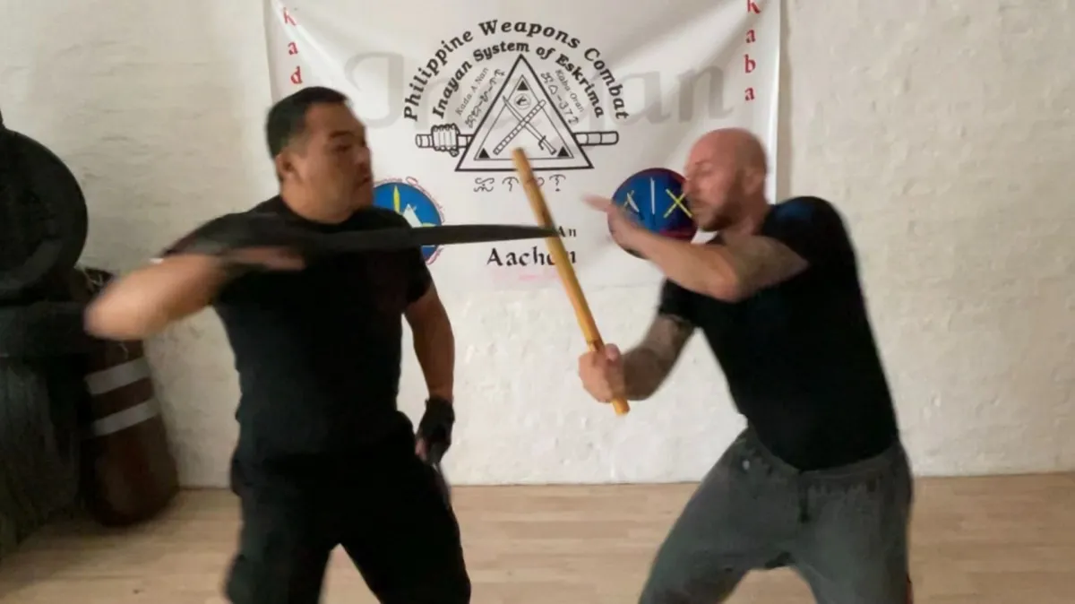 Stick and blade training in front of an Inayan System of Eskrima banner