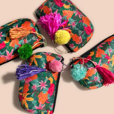 Four colorful Anna's travel bags each adorned with distinct tassels, displayed against a peachy background., 
