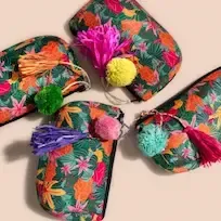 Four colorful Anna's travel bags each adorned with distinct tassels, displayed against a peachy background., 