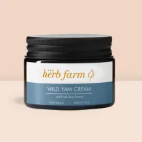 The Herb Farm Wild Yam Cream jar placed against a peachy background, accentuated by splashes of colorful paint for a vibrant look.