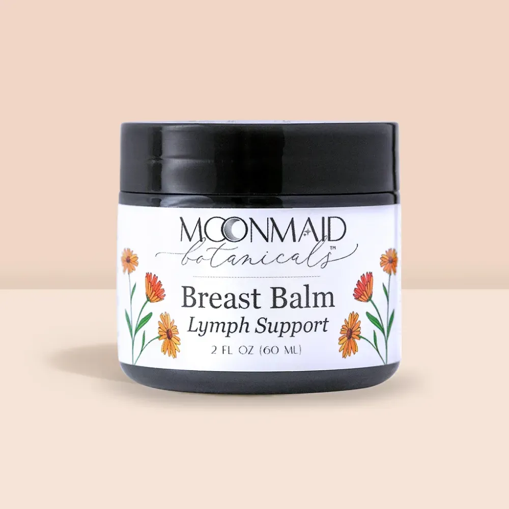 Product shot of MoonMaid Botanicals Breast Balm Lymph Support in a 2 fl oz (60 ml) dark glass jar against a soft peach background.