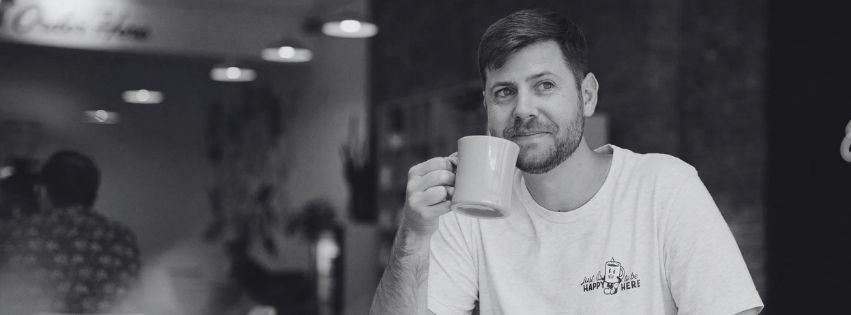 Tanner Olson Written to Speak, spoken word poetry and author, sips coffee and smiles at a coffee shop