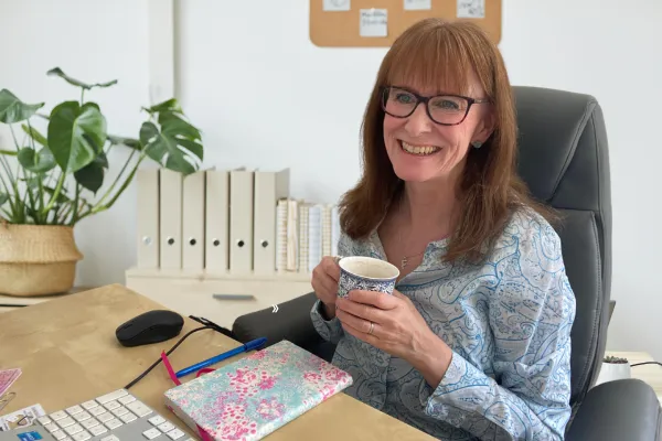 Fiona Dwyer, former TV journalist and PR coach, sitting at her desk holding a mug of tea while working on content.