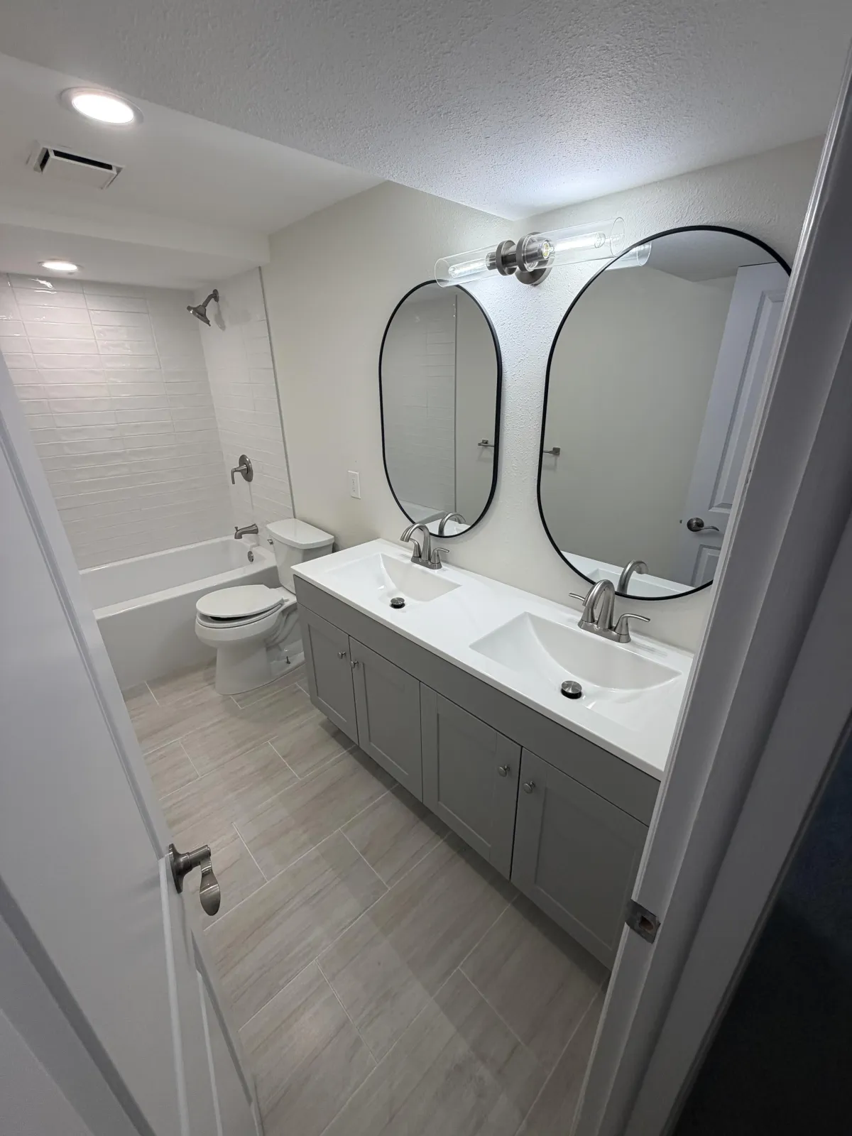 Bright, modern bathroom featuring a white freestanding bathtub next to a window, a dark wood vanity with a white top, and two mirrors.