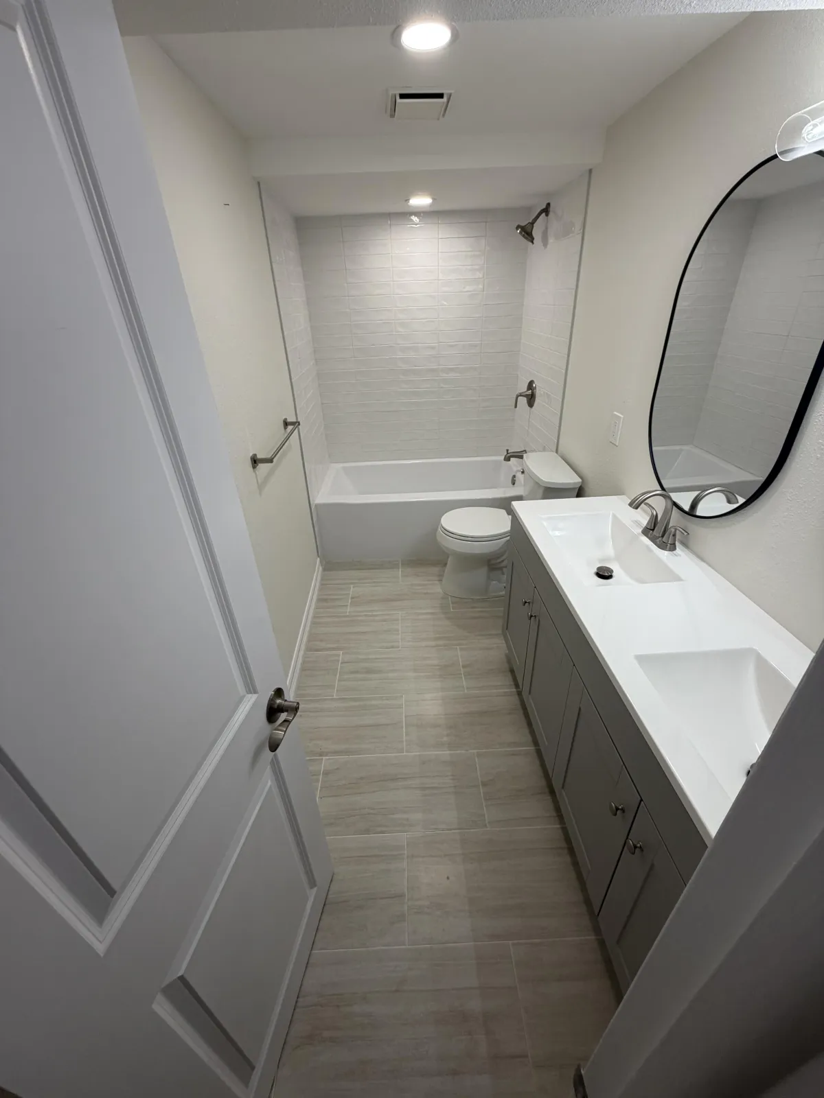 Clean bathroom view showing a light wood vanity with a plant, next to a large glass walk-in shower with black trim.
