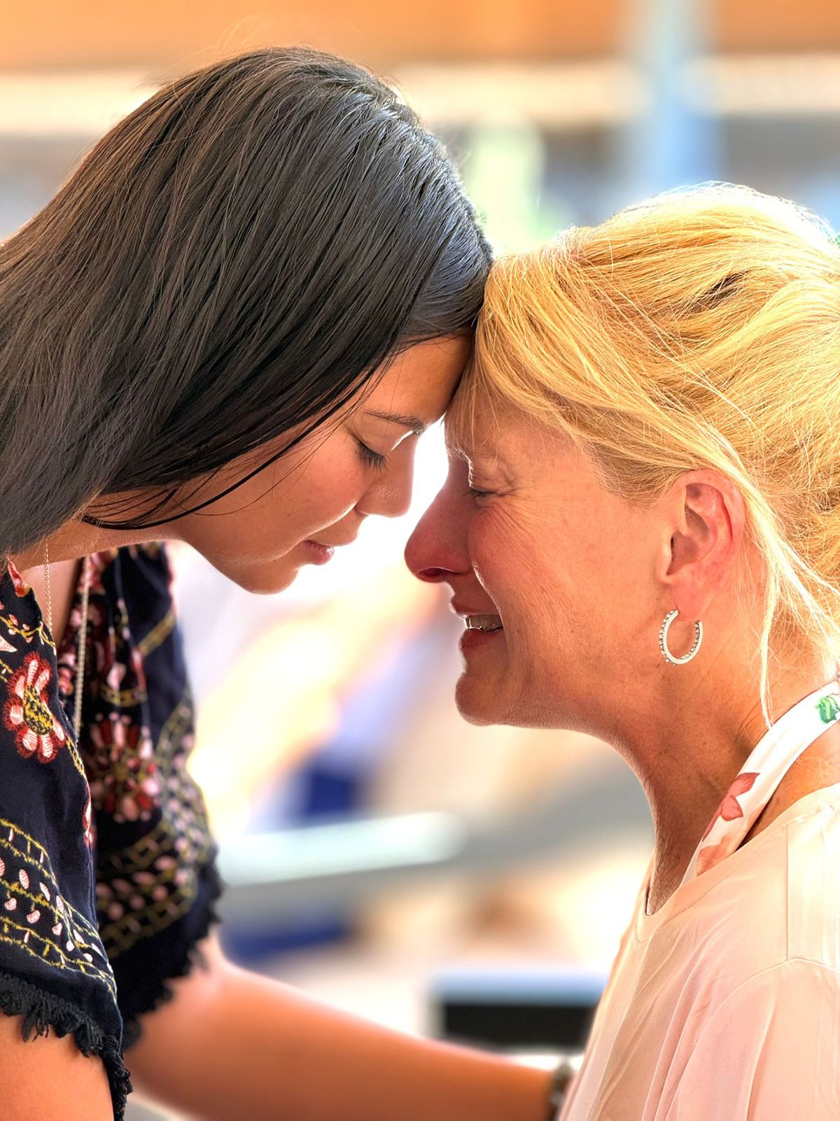 A serene indoor space with women seated in a circle, eyes closed, participating in a guided meditation session. Soft natural light filters through large windows, creating a peaceful and safe environment. The setting emphasizes tranquility, mindfulness, and the supportive nature of the retreat.