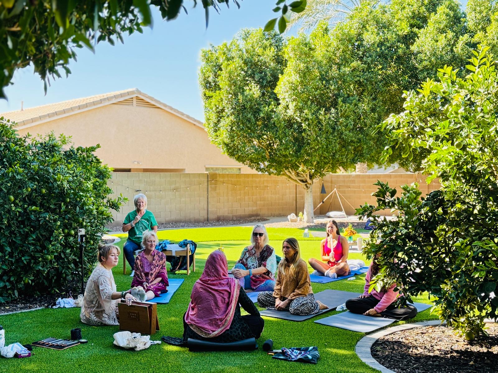 A serene indoor space with women seated in a circle, eyes closed, participating in a guided meditation session. Soft natural light filters through large windows, creating a peaceful and safe environment. The setting emphasizes tranquility, mindfulness, and the supportive nature of the retreat.