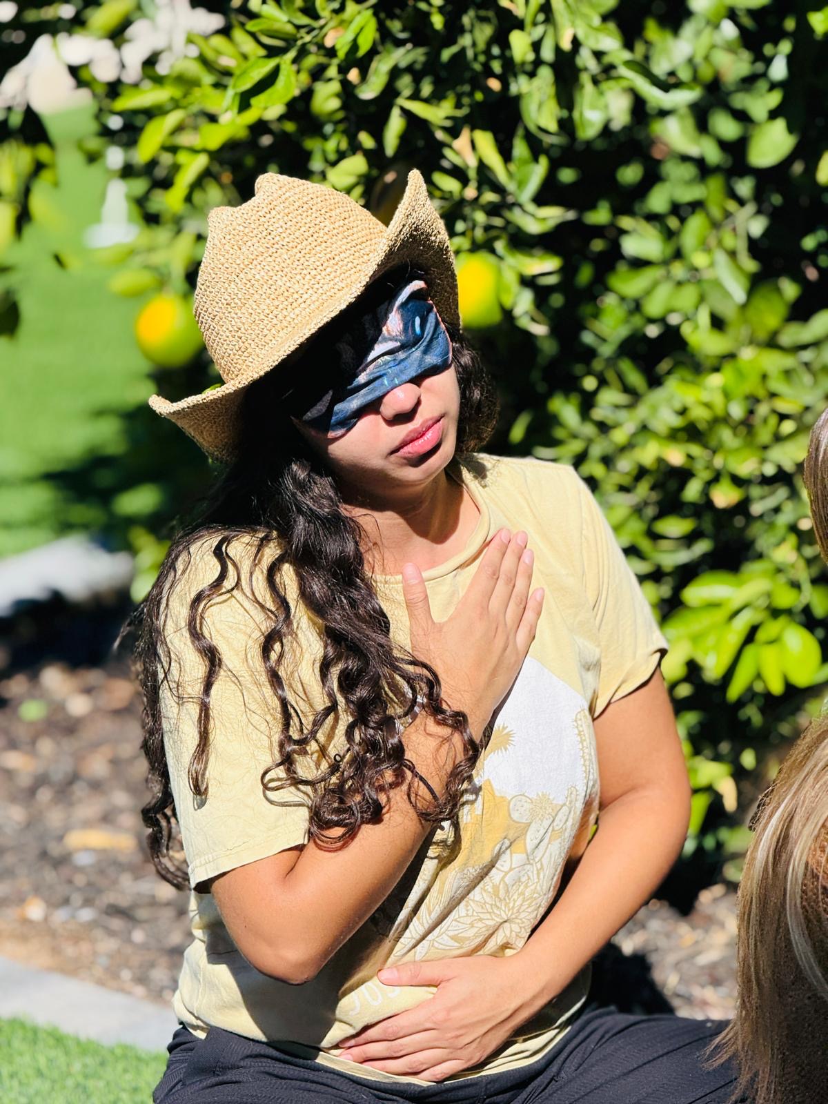 A group of women in a sunlit garden, holding hands in a circle, eyes closed, participating in a group breathwork session, surrounded by blooming flowers and greenery.