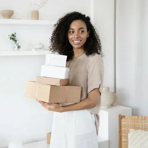 Smiling homeowner holding stacked boxes inside bright modern home
