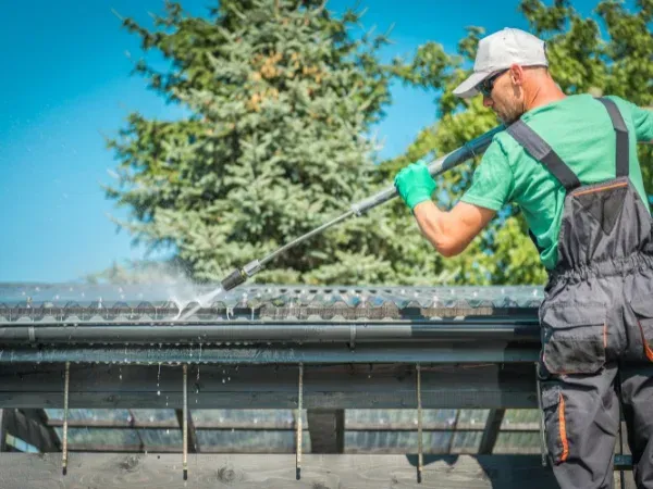 Worker cleaning a house gutter using a pressure washer for maintenance