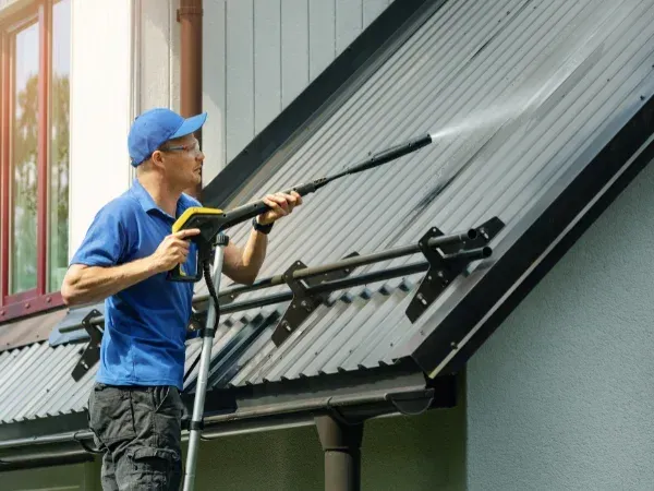 Worker pressure washing a residential metal roof for cleaning