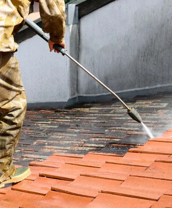 Worker pressure washing red clay roof tiles to remove moss and stains