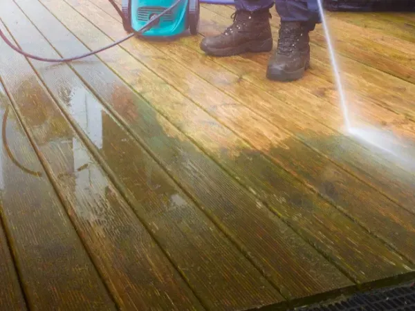 Deck being cleaned with a power washer, showing before and after contrast