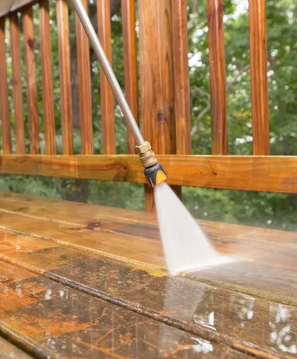 Close-up of pressure washing wooden deck railing for maintenance.