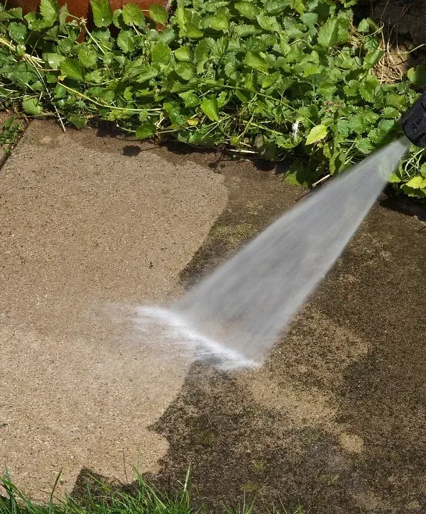 Pressure washing patio — cleaning dirt and moss from concrete surface with high-pressure water.