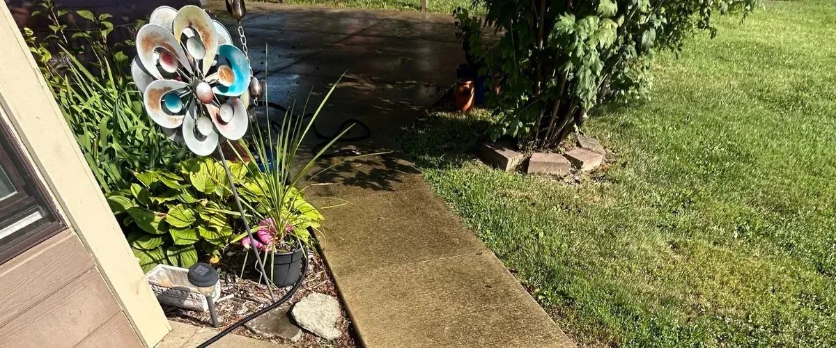 Garden walkway freshly pressure washed, with surrounding plants, yard decor, and patio area visible in the background.
