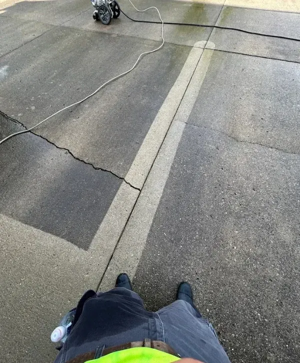 Pressure washing concrete driveway showing clear cleaning lines and surface restoration.
