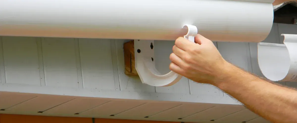 Installing PVC rain gutter bracket on residential home exterior.