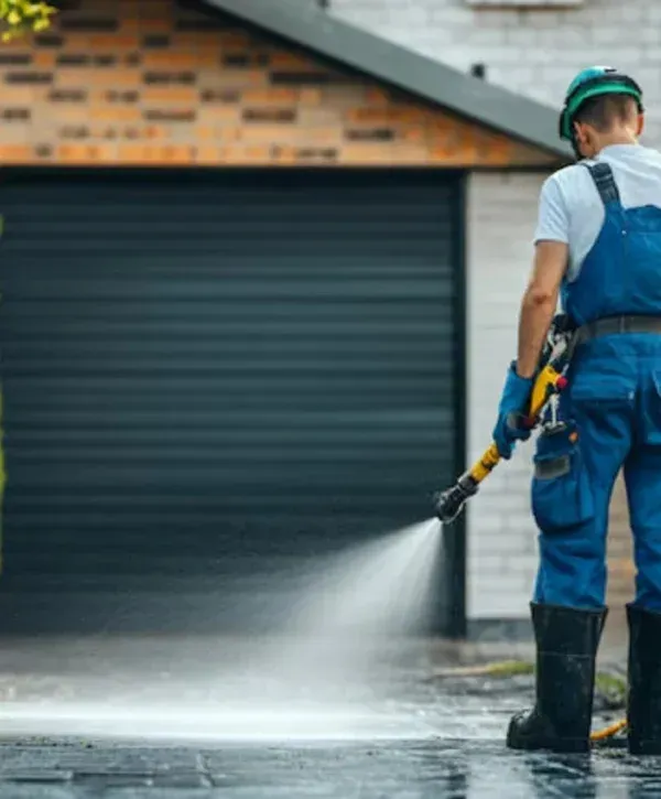 Technician pressure washing driveway surface in front of garage.