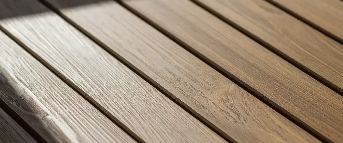 A close-up, high-angle view of weathered wooden decking planks, showing natural grain and texture.