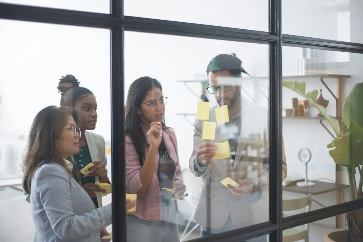 A multi-national group of employees gather around a window strategizing