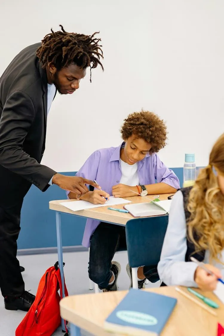 African American teacher leans over desk helping student succeed