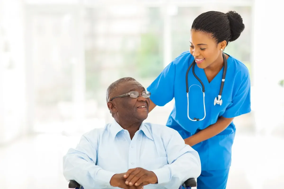 A smiling elderly man in a wheelchair with a caring nurse, representing peace of mind after receiving justice for harmful drug injuries.