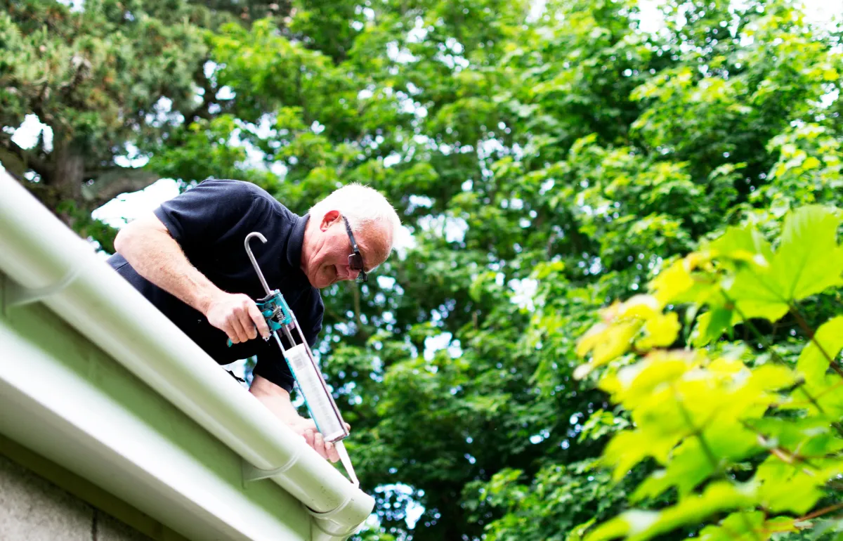 Technician sealing and aligning gutters on a home, showcasing professional gutter maintenance for long-lasting protection.