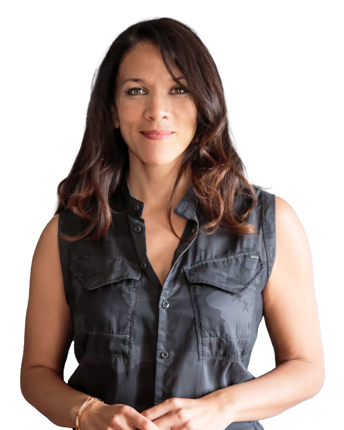 A woman with shoulder-length dark hair, wearing a sleeveless black shirt with buttoned pockets, standing in front of a plain gray background. She is smiling gently and has her hands clasped in front of her.