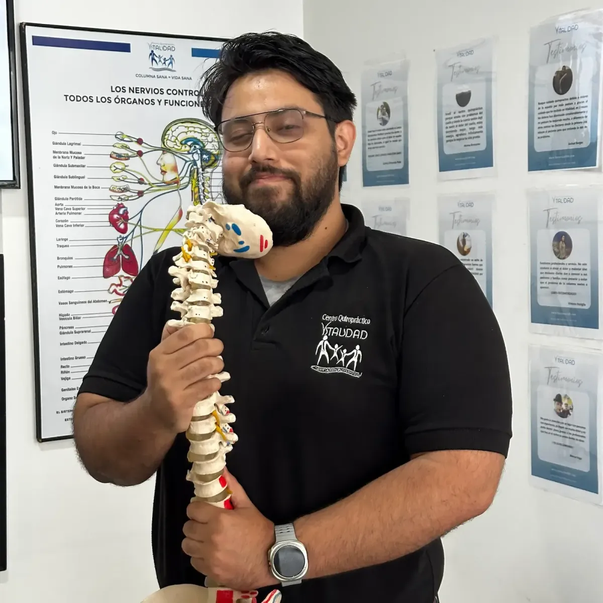 Dr. Méndez sonriente sosteniendo una columna vertebral con fondo del sistema nervioso y testimonios de pacientes, mostrando resultados reales de la quiropráctica en Centro Quiropráctico Vitalidad