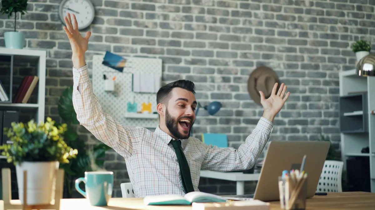 A man celebrating something at his laptop in the office.