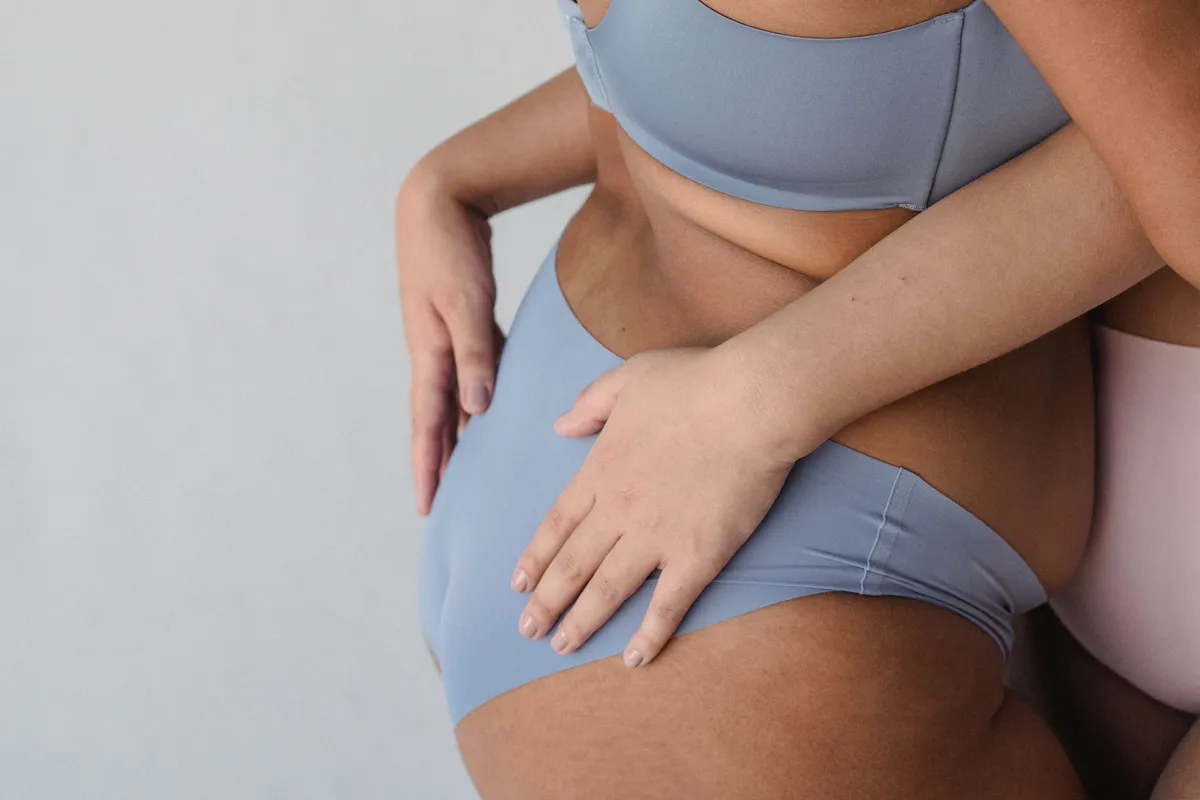 Two women wearing underwear sitting closely together, representing vaginal health, intimate wellness, and the factors that influence the vaginal microbiome and pH.