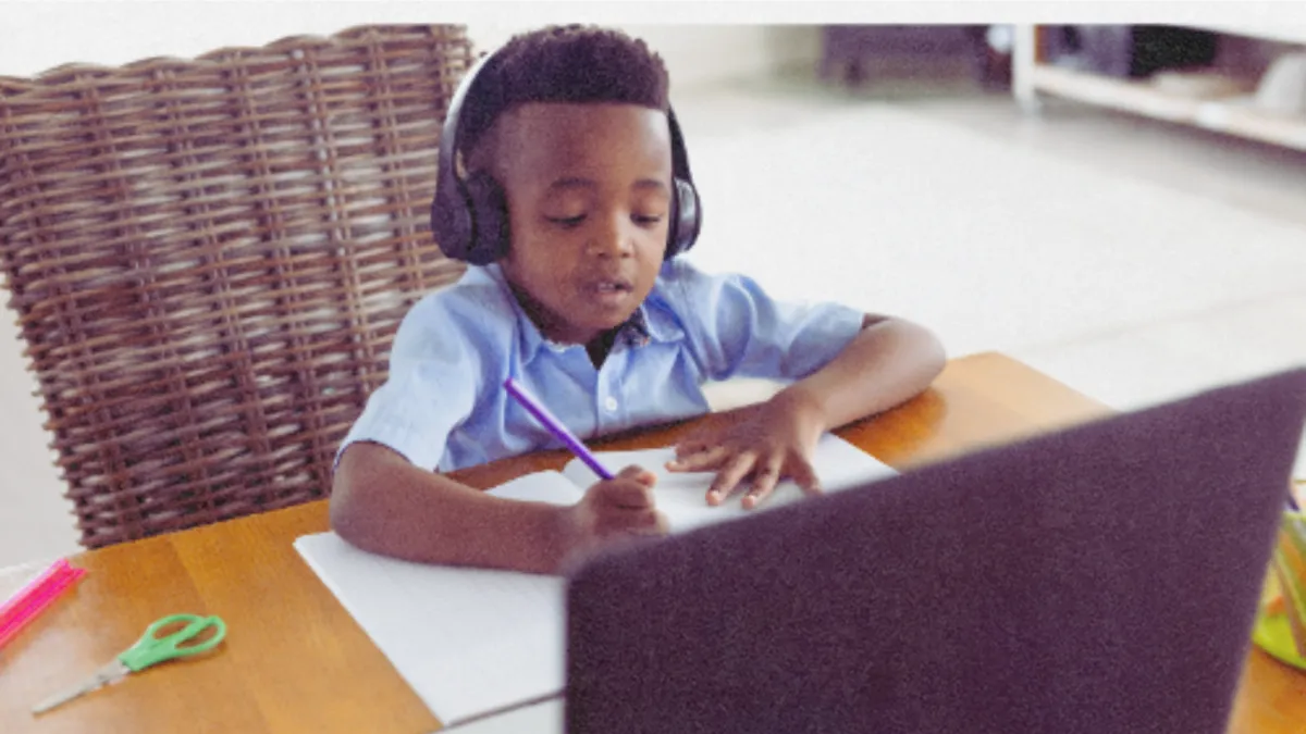 Child with headset smiles as he engages with laptop