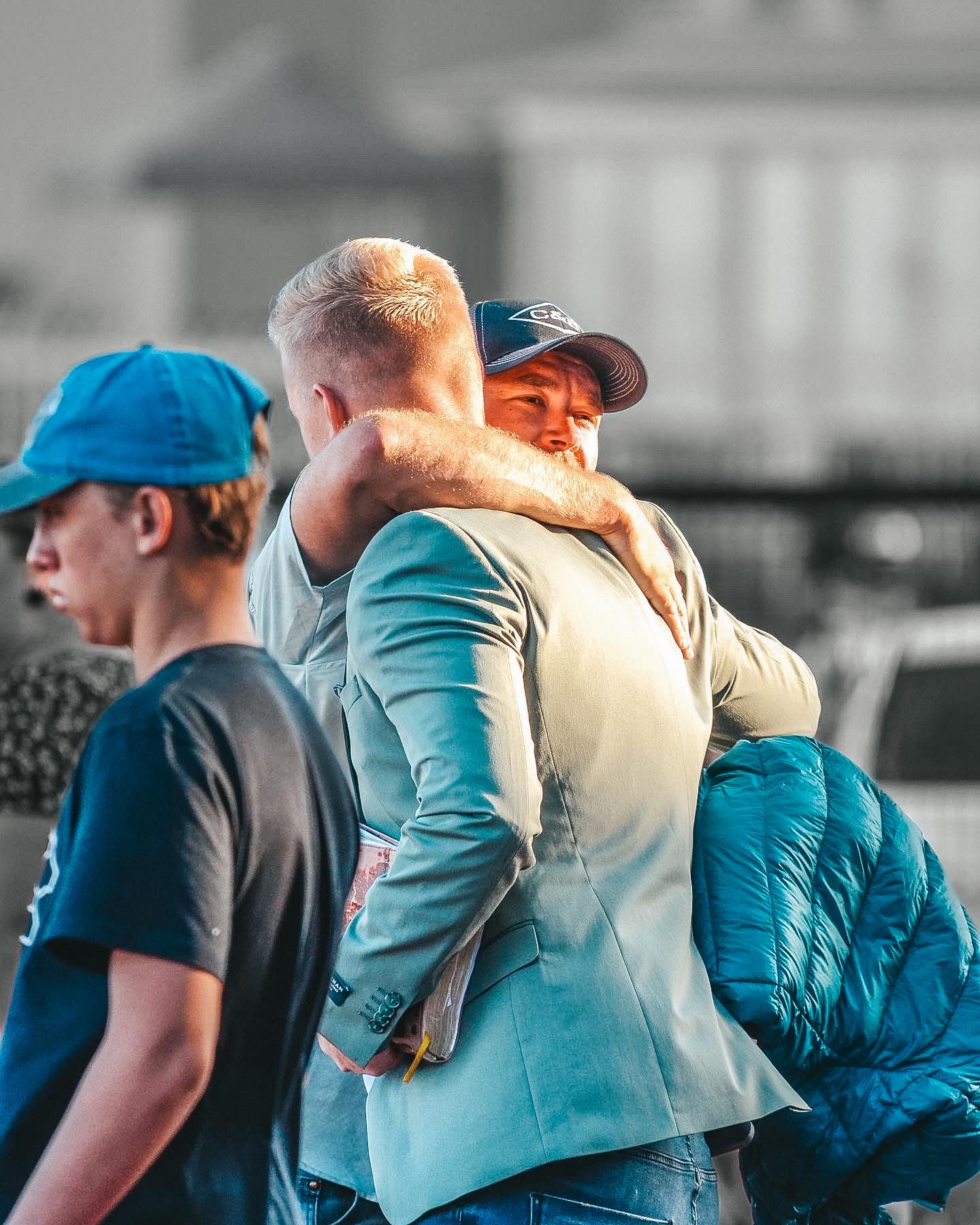 A close-up of two hands gently holding a small wooden cross, with soft sunlight streaming through a window. The hands belong to different generations, symbolizing faith, hope, and unity across ages.