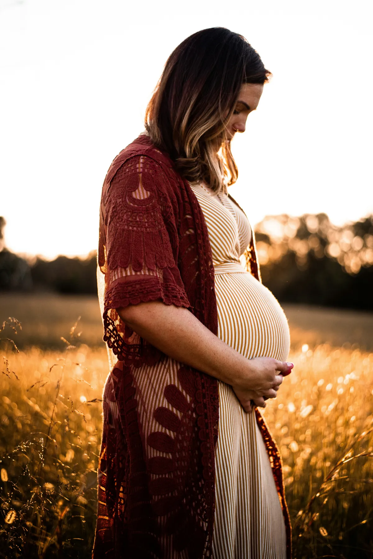 Silhouette of a pregnant woman standing on a beach at sunrise or sunset, reflecting on wet sand.