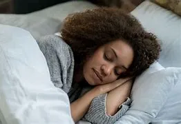 A woman with curly hair peacefully sleeping in bed, representing the importance of quality rest.