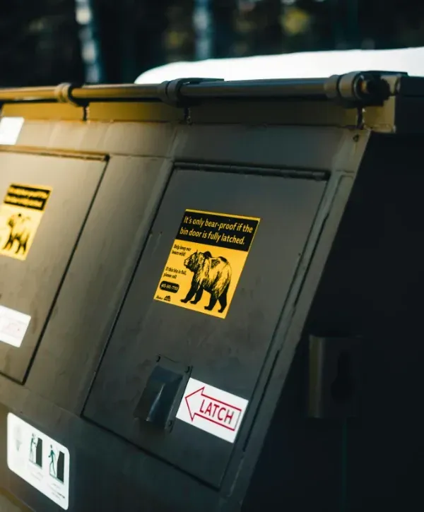 Bear-proof trash bin with wildlife warning sign and latch instruction label.