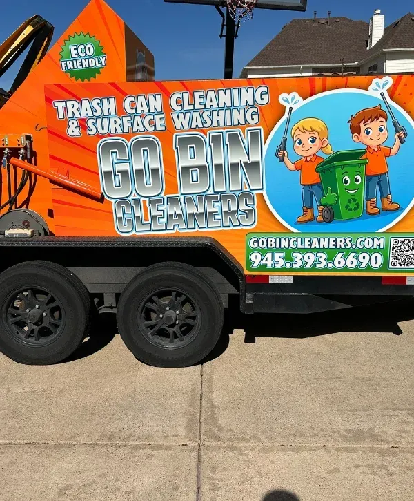 A blue GoBin Cleaners truck with cartoon characters on the side, parked in front of four blue and green bins.