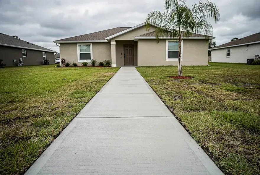 Freshly poured concrete sidewalk along the front yard of a Lake Worth, Florida home on an overcast day.